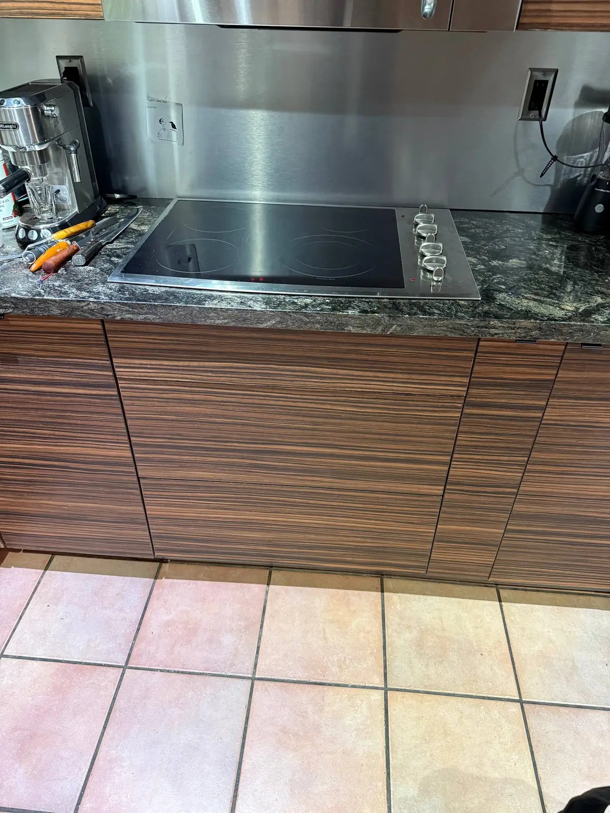 A cooktop on a granite countertop with a coffee machine and tools nearby