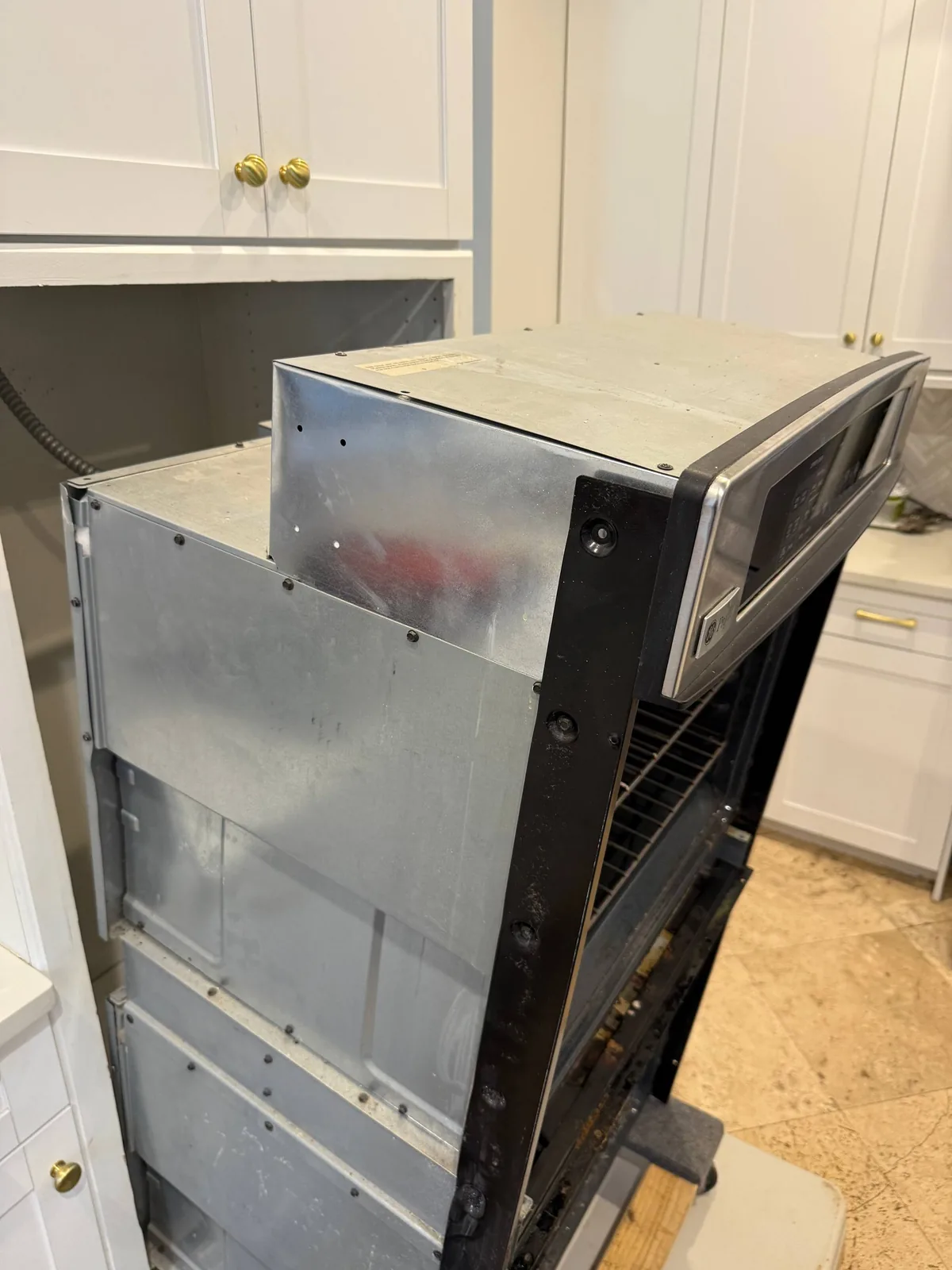 A disassembled oven with its metal casing exposed, next to kitchen cabinetry