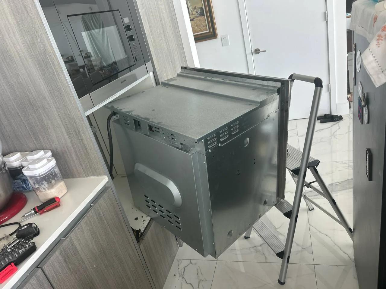 An oven is pulled out of its cabinet during repair, with tools visible on the counter