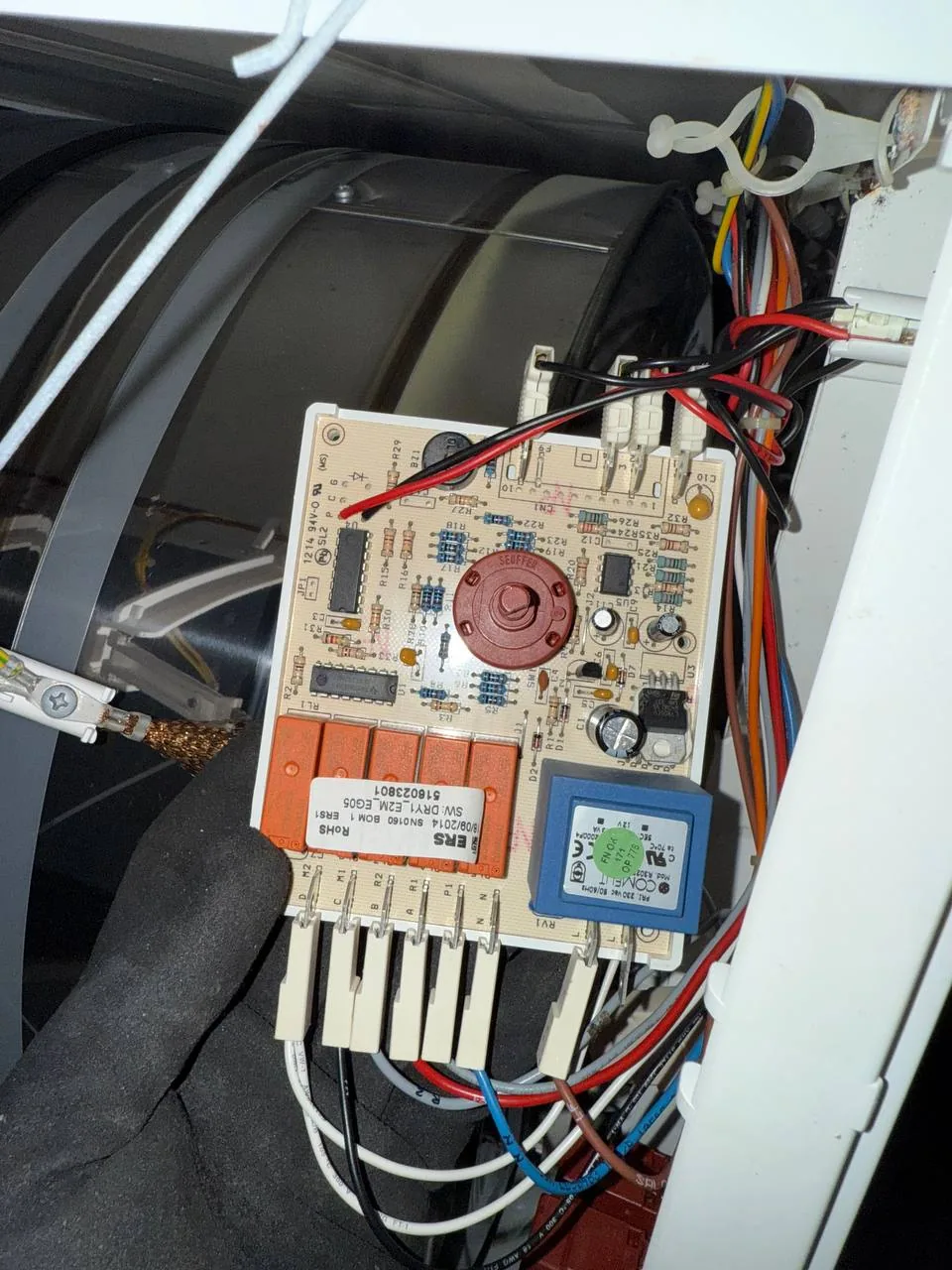 A technician's gloved hand next to a dryer's control board and wiring