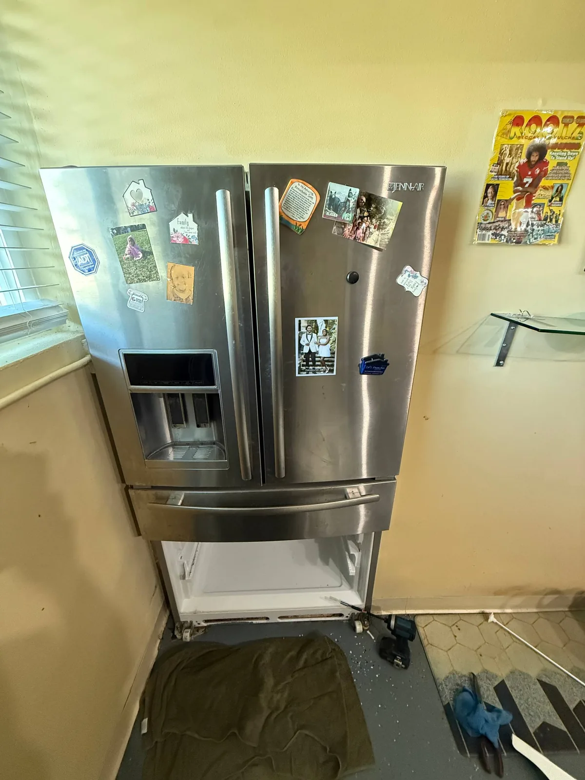 A stainless steel JennAir refrigerator with the freezer drawer open, and tools on the floor indicating a repair in progress