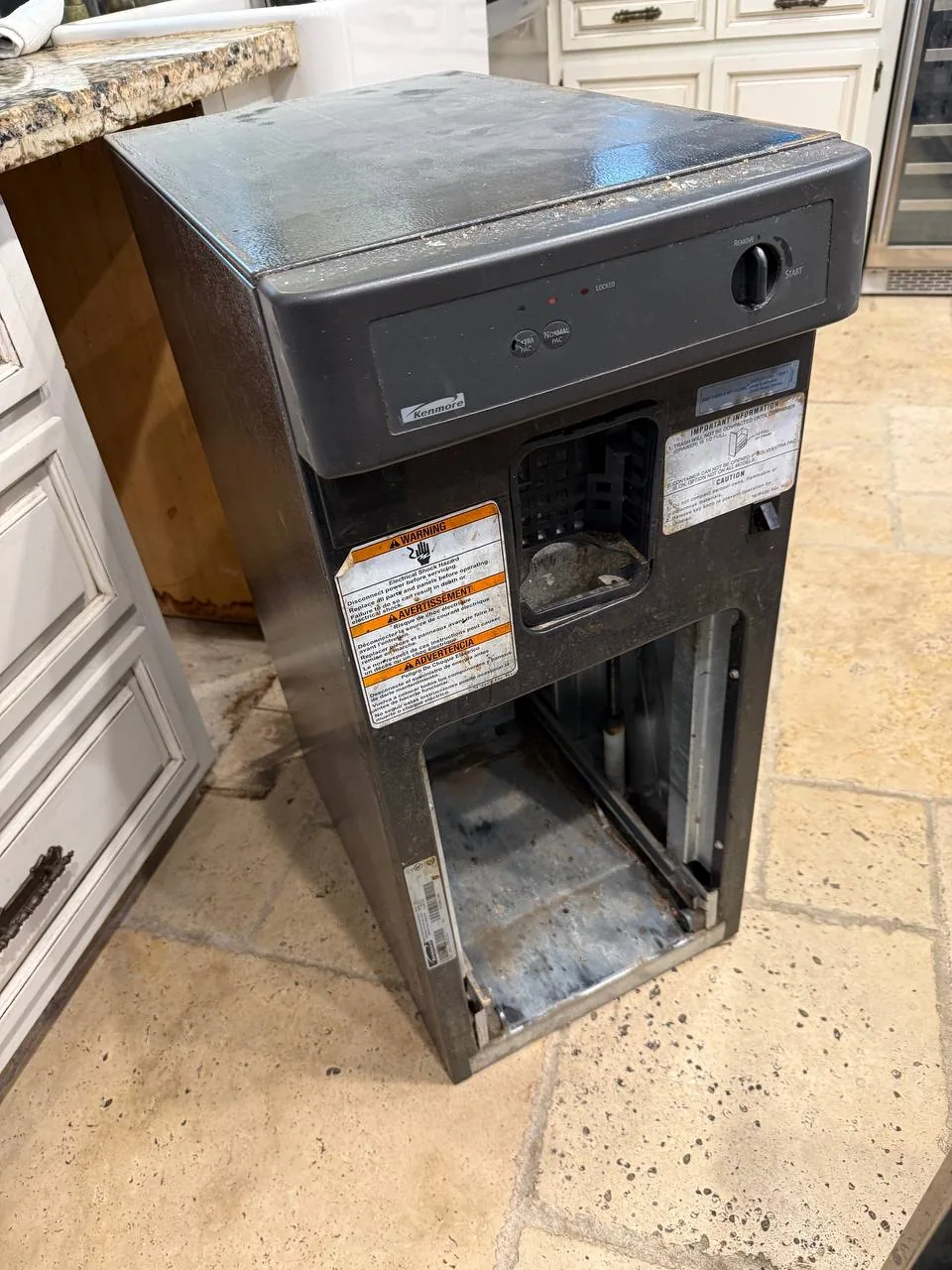 A Kenmore dishwasher, removed from its under-counter space, sits on a tiled kitchen floor