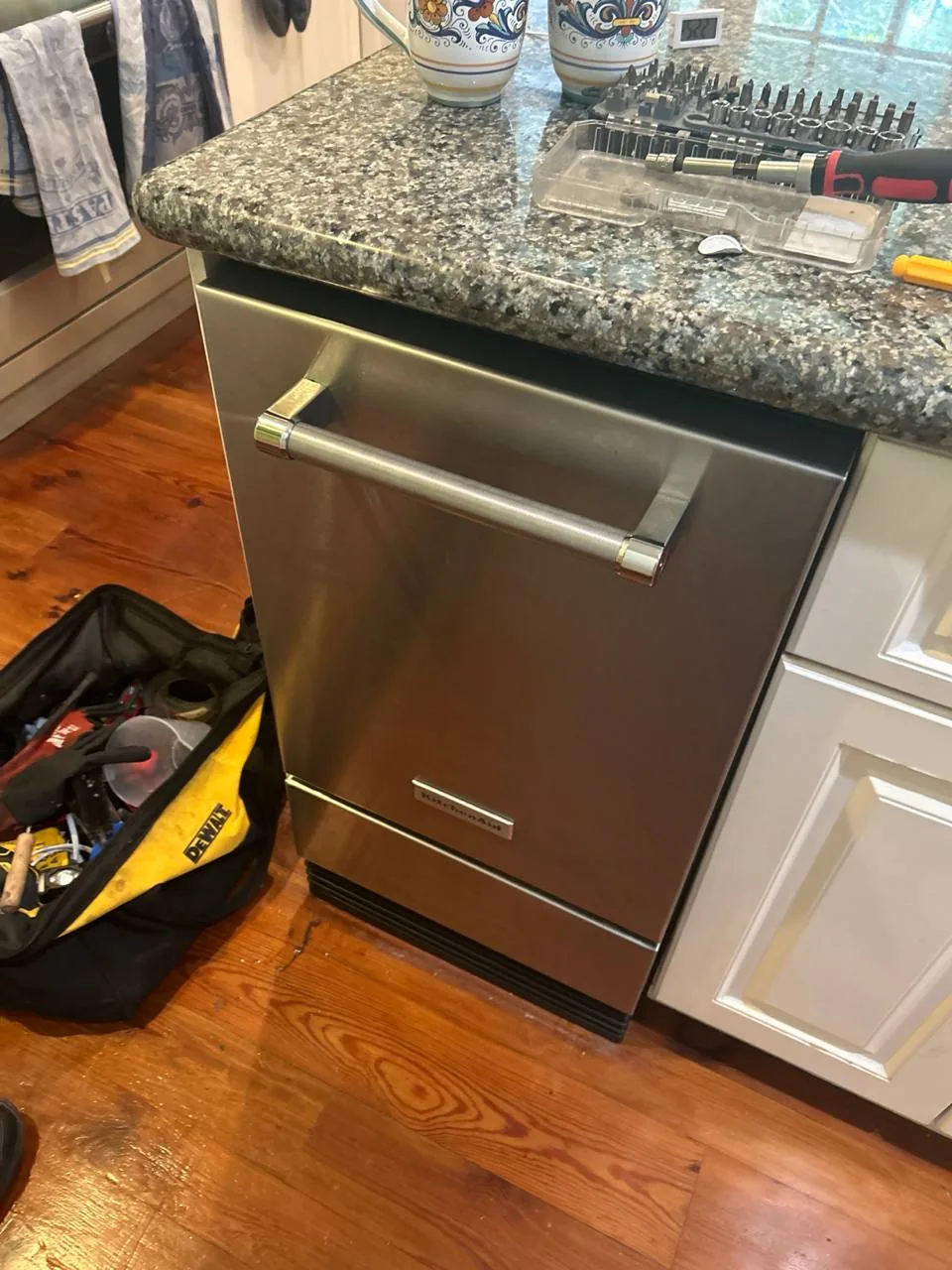 A stainless steel KitchenAid dishwasher with a Dewalt tool bag and screwdriver set nearby on the counter