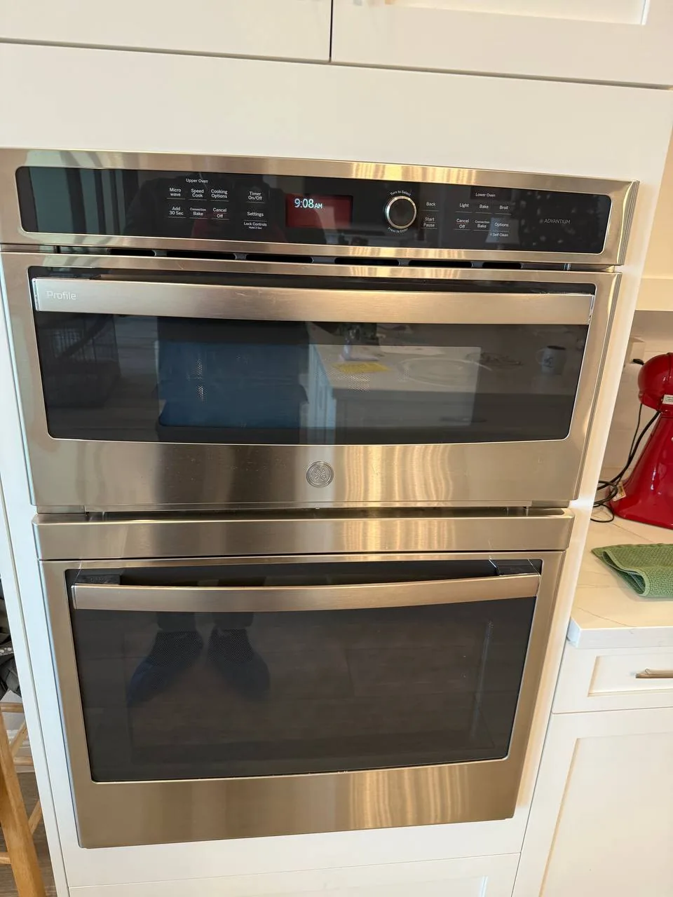 A stainless steel double oven, with a reflection of a technician's feet in blue shoe covers