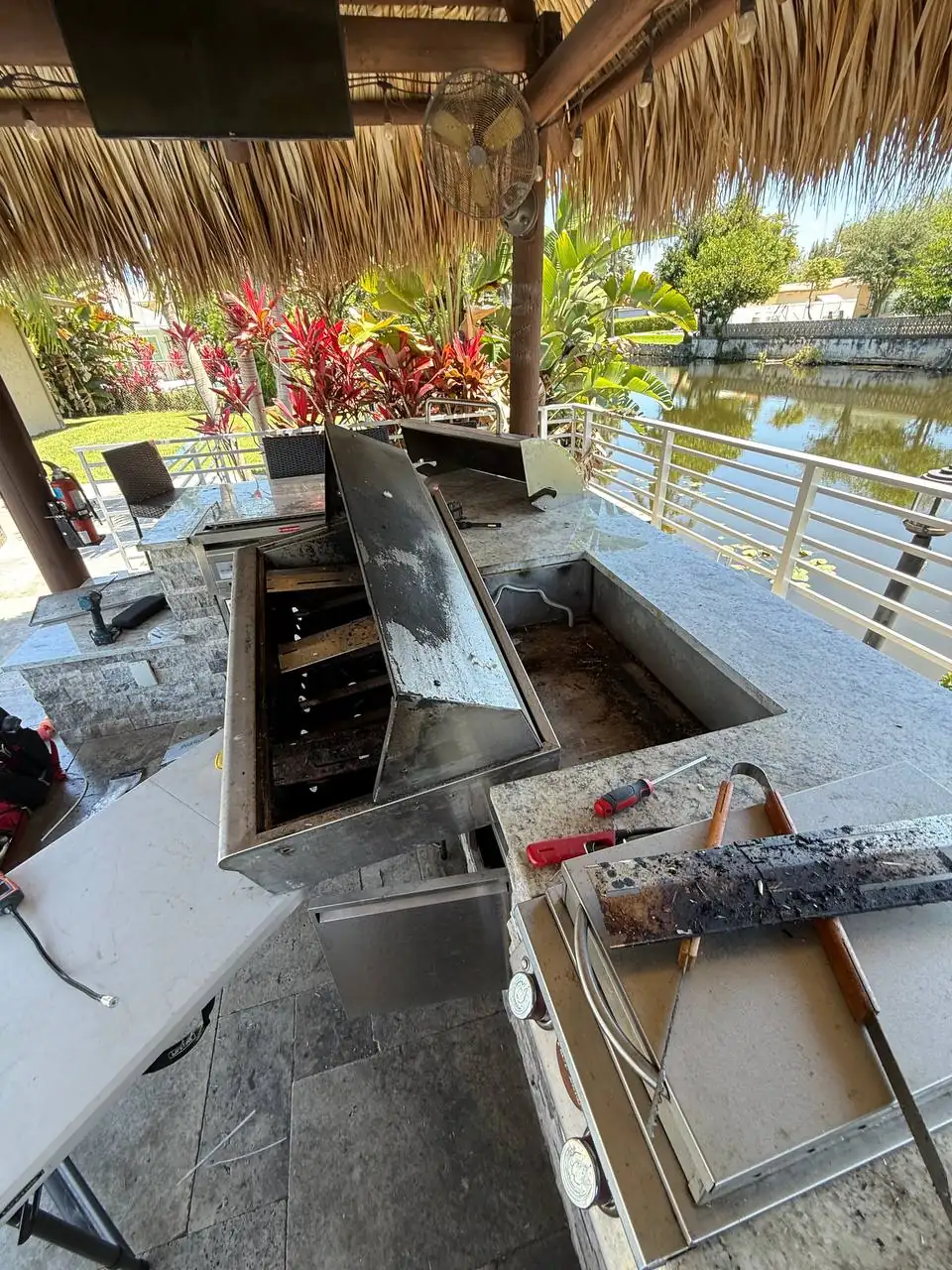 An outdoor kitchen area with a partially disassembled cooktop, tools, and a view of a body of water