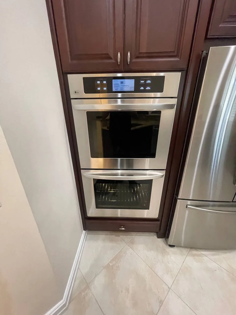 A stainless steel double oven installed in kitchen cabinetry next to a refrigerator