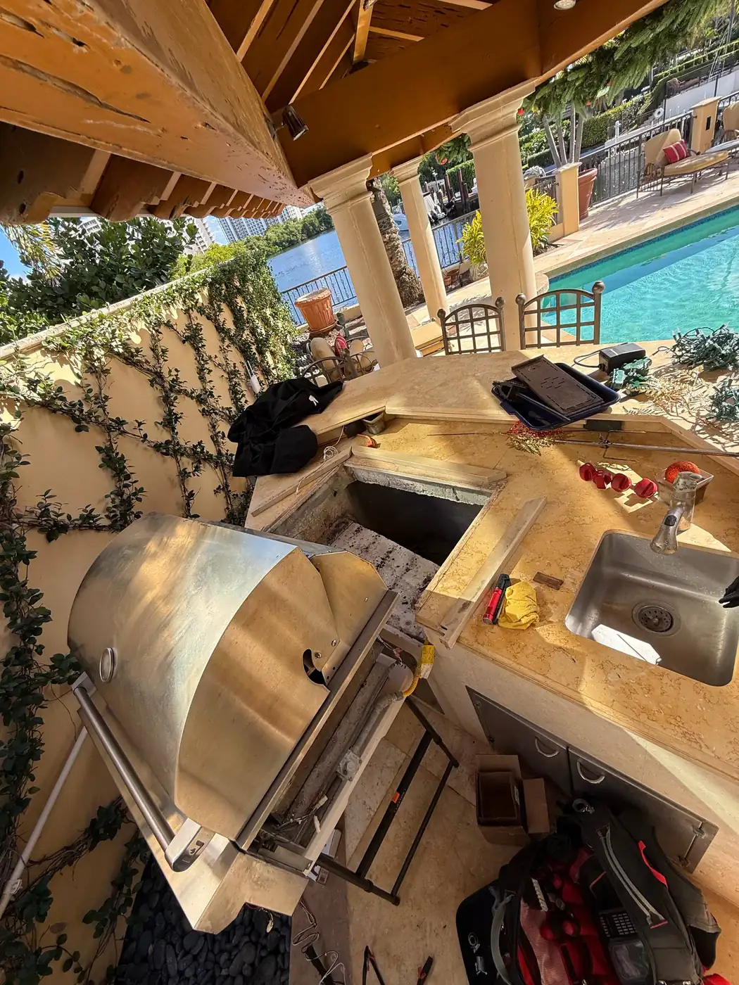 A stainless steel outdoor grill next to an outdoor sink, with a large open space in the countertop indicating a repair or
