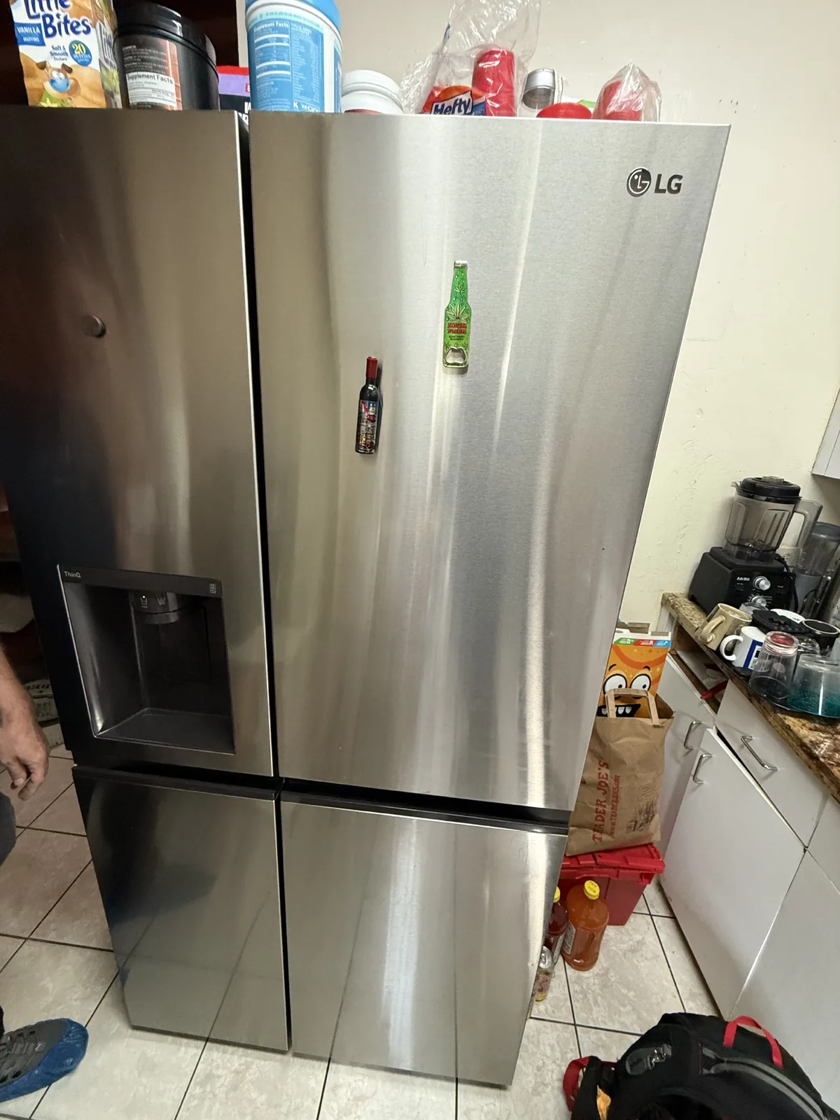 A technician's foot next to a stainless steel LG refrigerator with magnets on the door