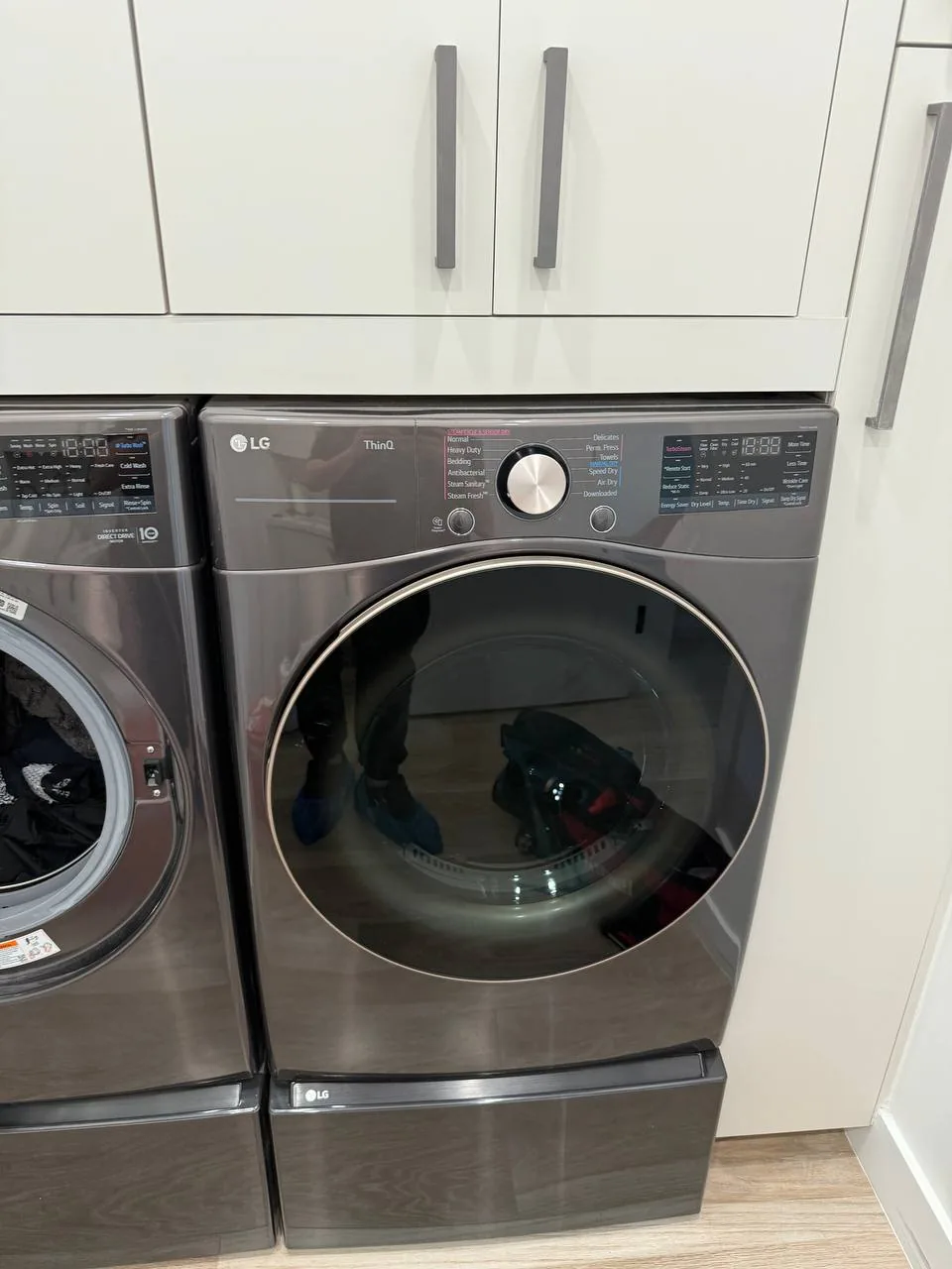 A modern gray LG dryer with a reflection of a technician's feet in blue shoe covers