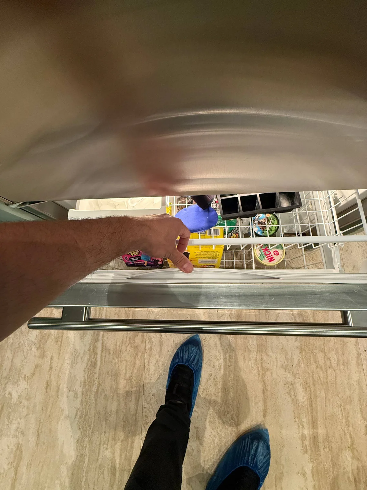 A technician wearing blue shoe covers is reaching into a stainless steel refrigerator