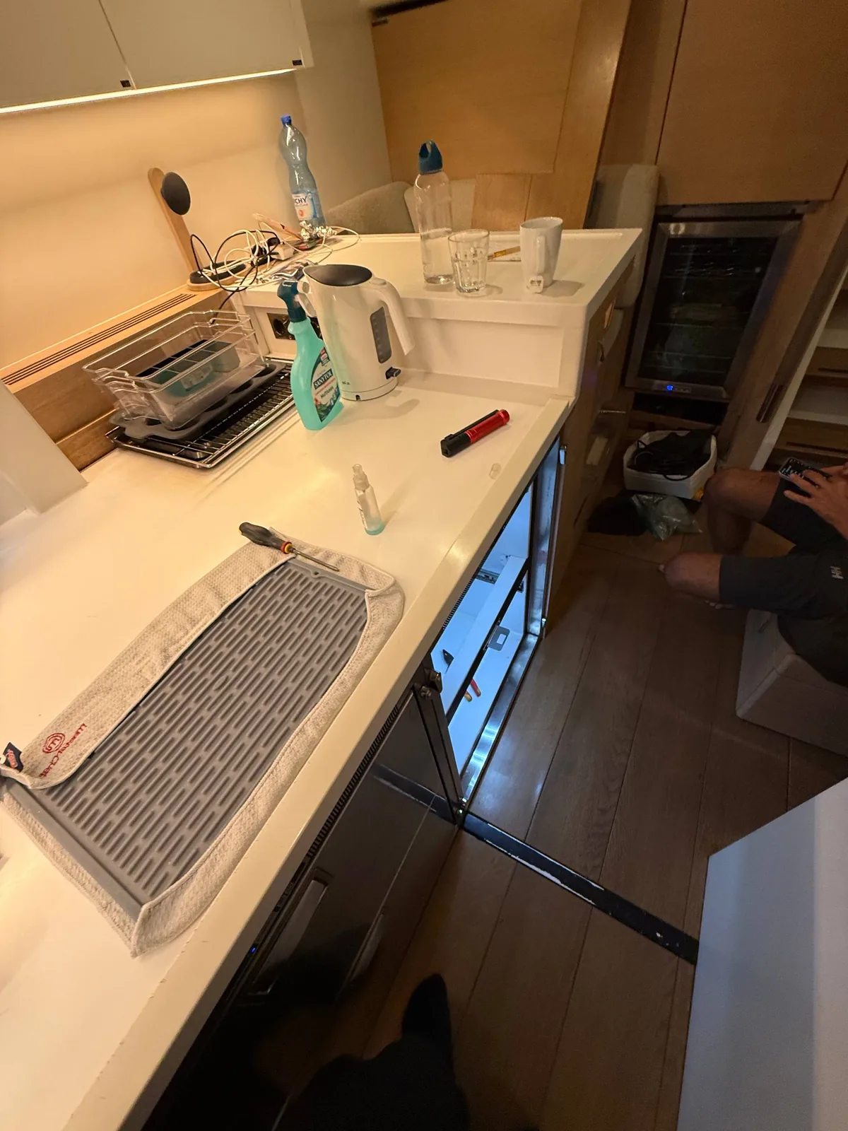 A wine cooler and a technician's legs in a kitchen setting with tools on the counter