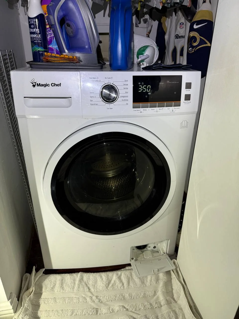 A white Magic Chef washing machine with its bottom panel open, sitting on a white towel