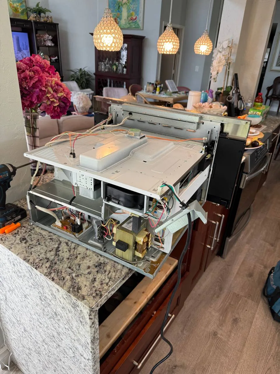 A microwave is disassembled on a kitchen counter for repair