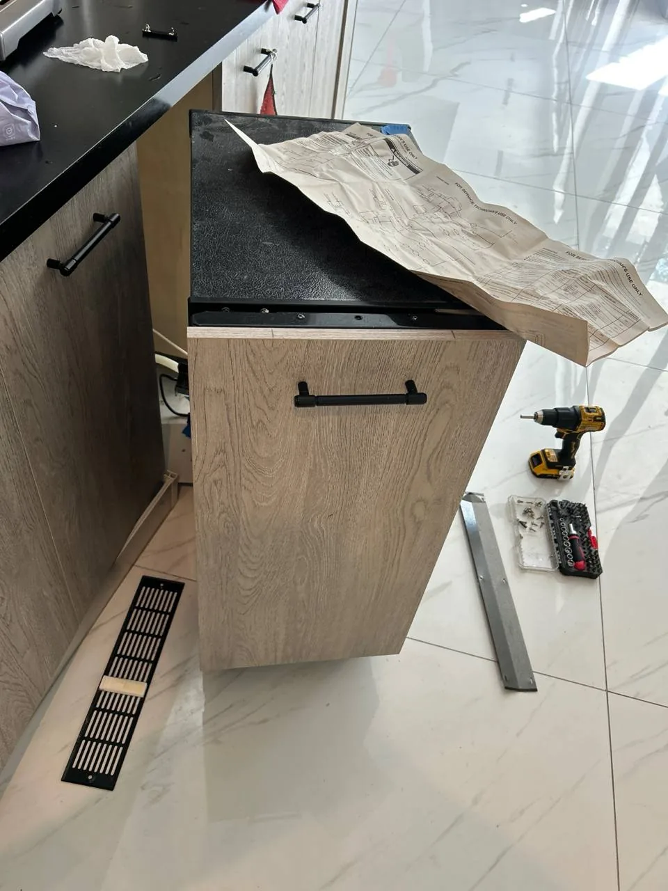 A wine cooler in a modern kitchen setting, with tools and a schematic document nearby