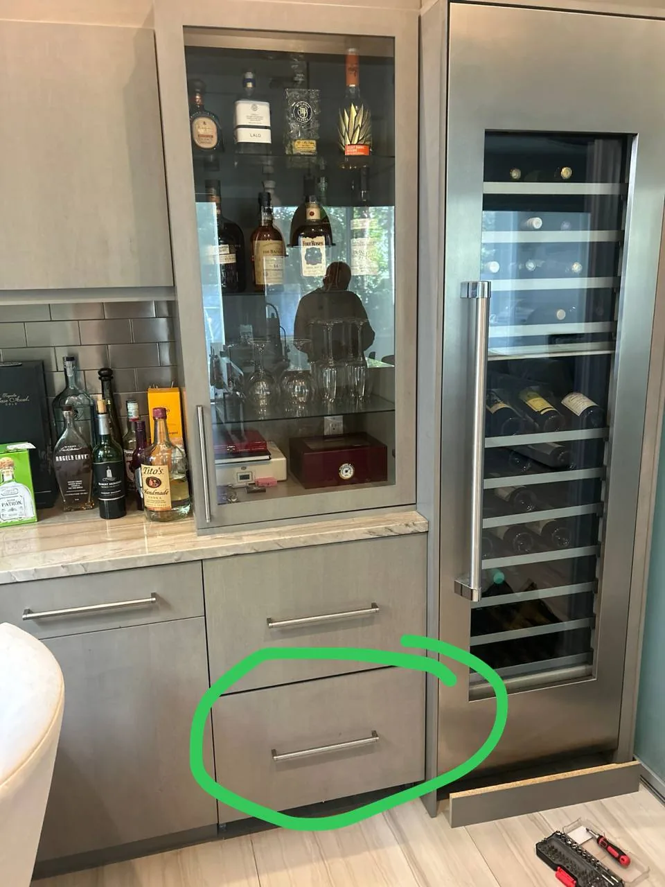 A wine cooler next to cabinetry, with a reflection of a technician visible in the glass