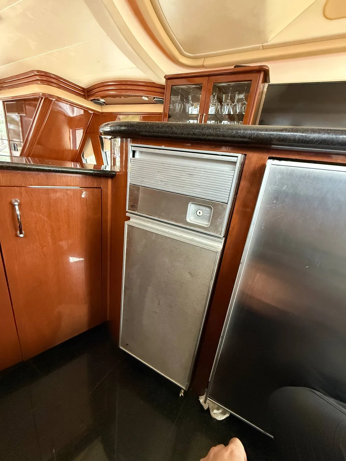 A stainless steel ice maker is installed under a counter with a wooden cabinet and dark countertop