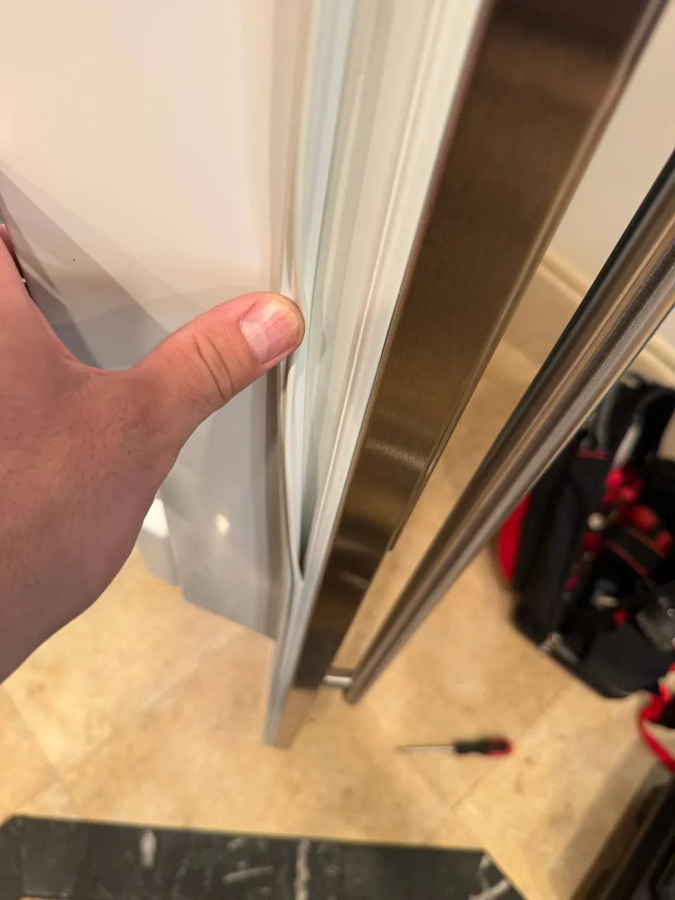 A technician's hand pressing on the seal of a white refrigerator with a stainless steel handle