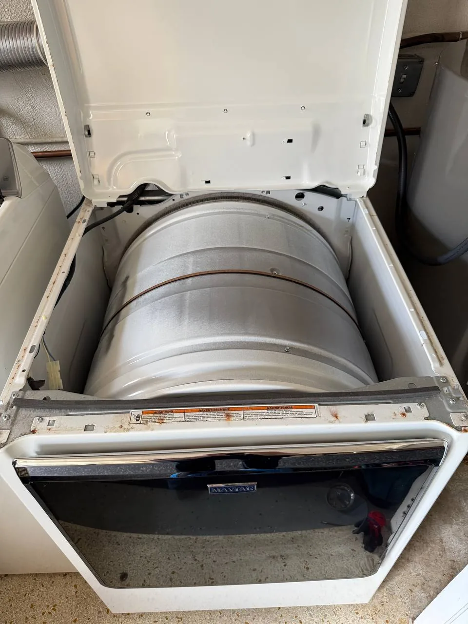 The a disassembled Maytag dryer, with the top panel lifted to reveal the drum inside, indicating a repair in progress