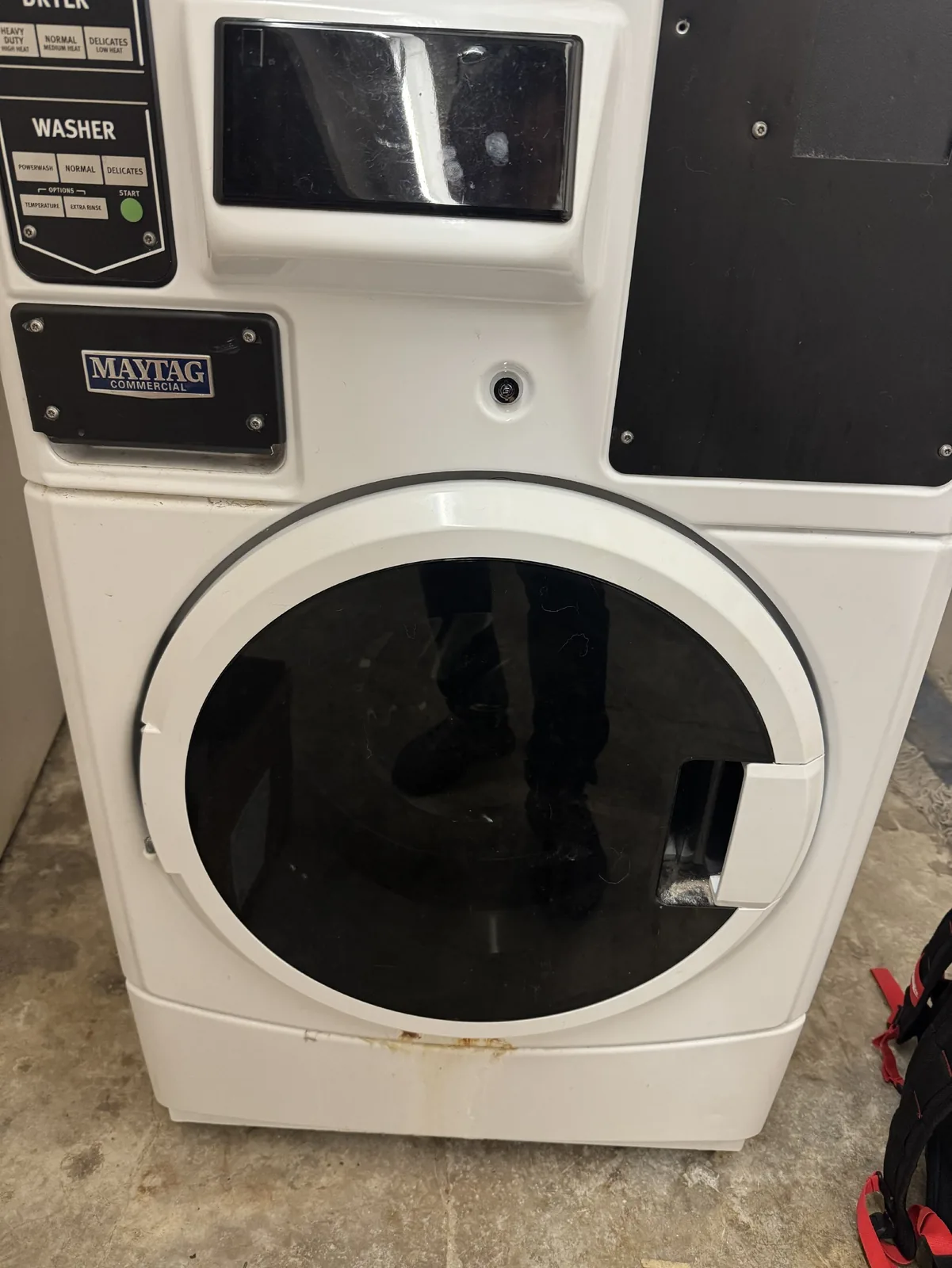 A reflection of a technician in the washer's door, showing a Maytag Commercial washer