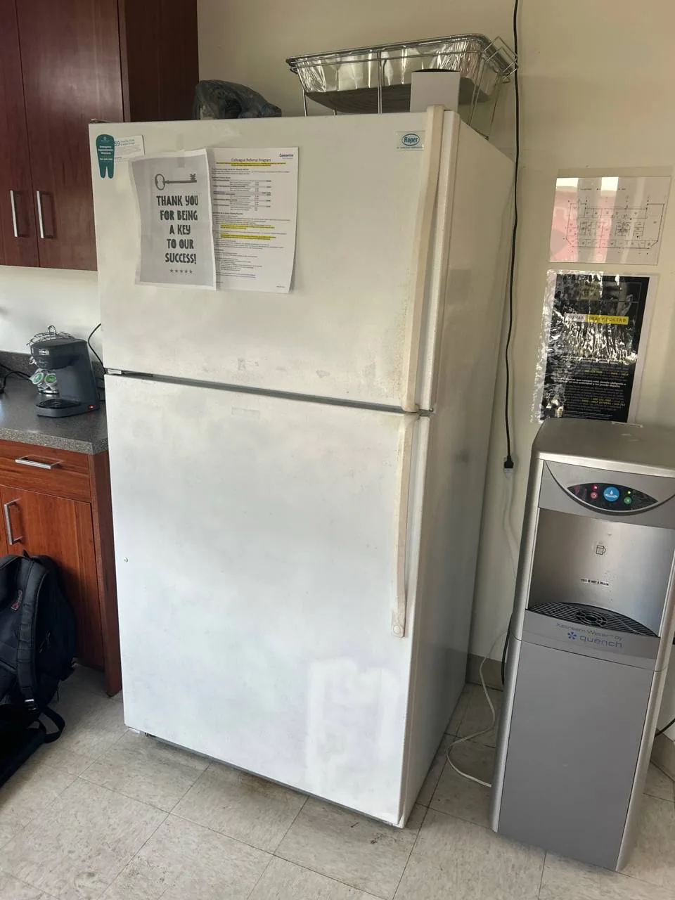 A white Roper refrigerator with papers on the door, next to a water cooler