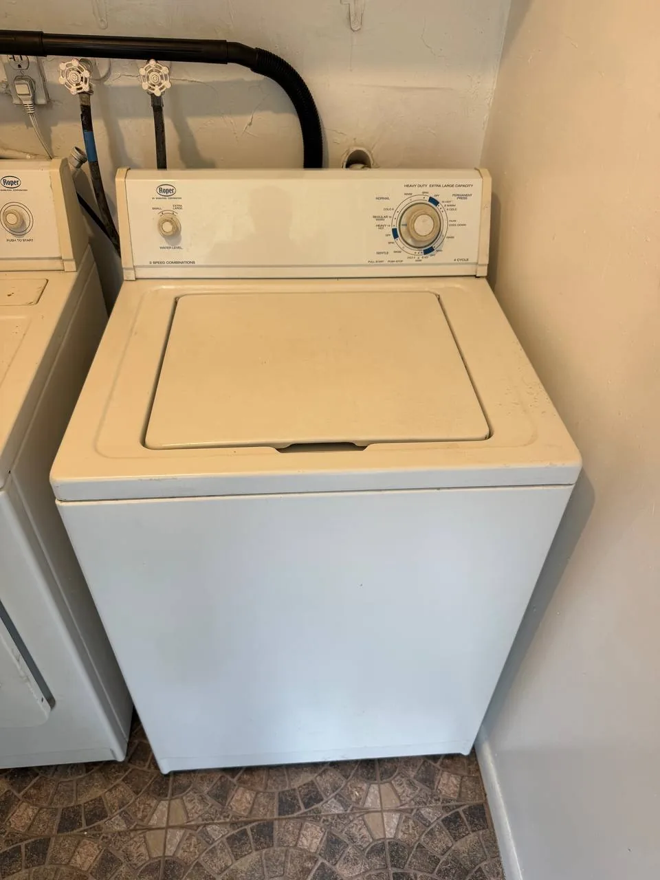 A white Roper washing machine in a laundry room with a second washing machine to its left
