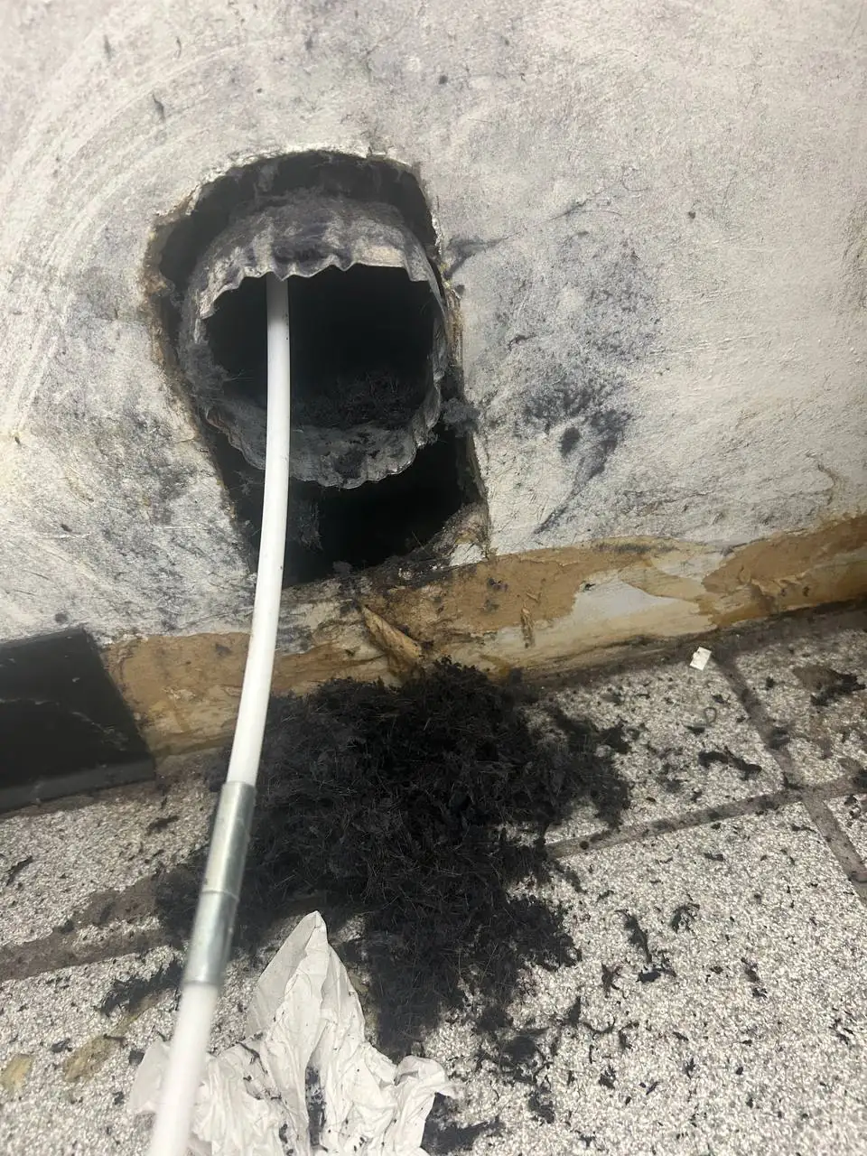 A dryer vent cleaning tool in a vent opening, next to a large pile of lint removed from the dryer duct
