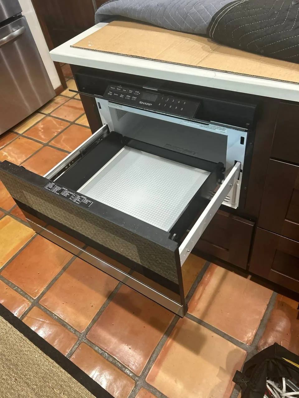 A Sharp drawer-style microwave oven installed in a kitchen island with its drawer open
