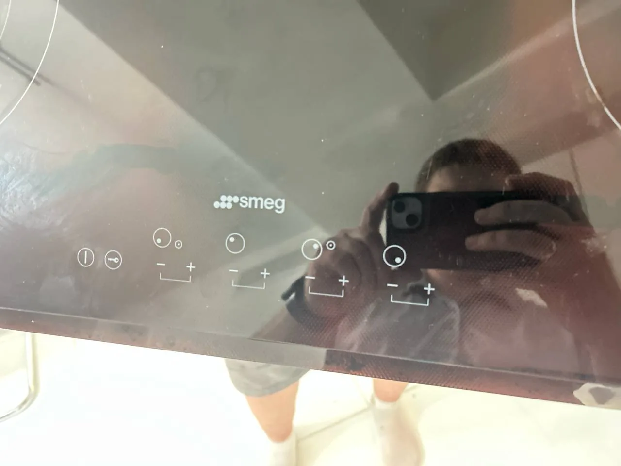 A reflection of a technician taking a a Smeg cooktop