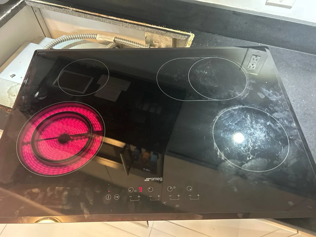 A dirty Smeg induction cooktop with one burner glowing red
