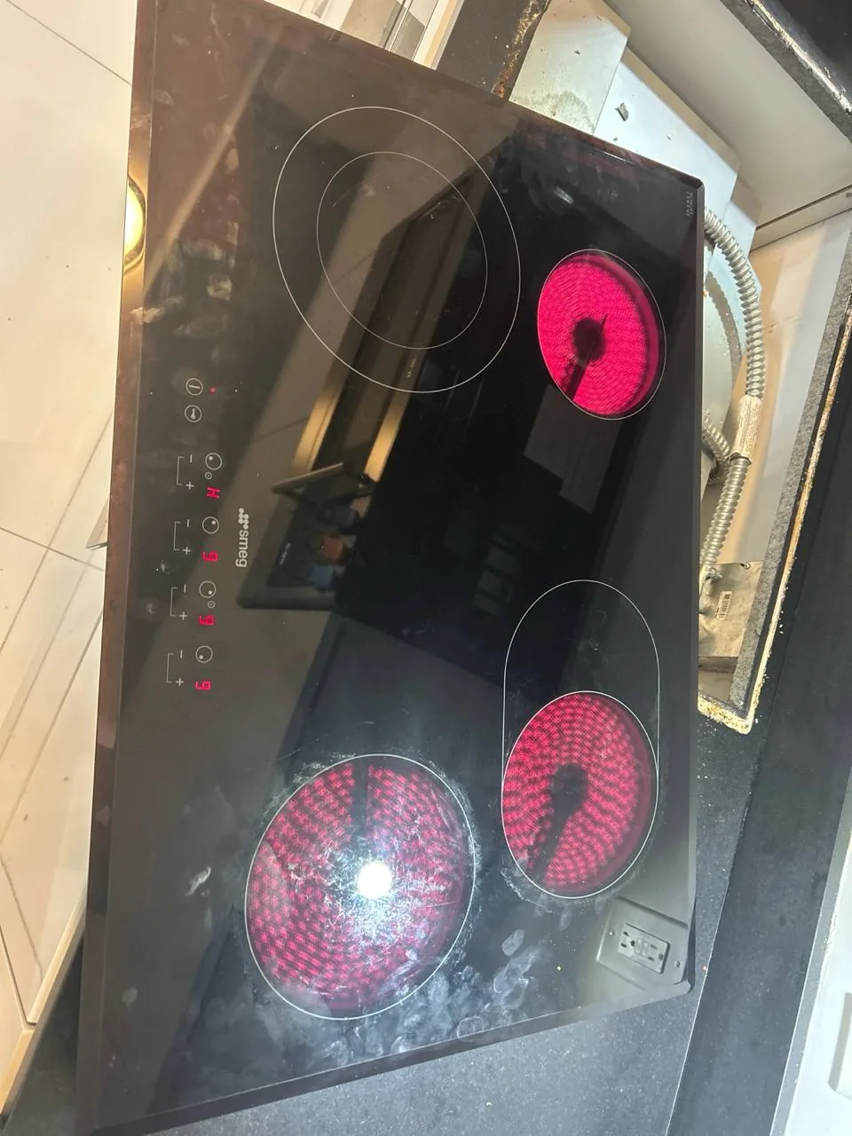 A Smeg electric cooktop with three burners, two of which are glowing red, from above