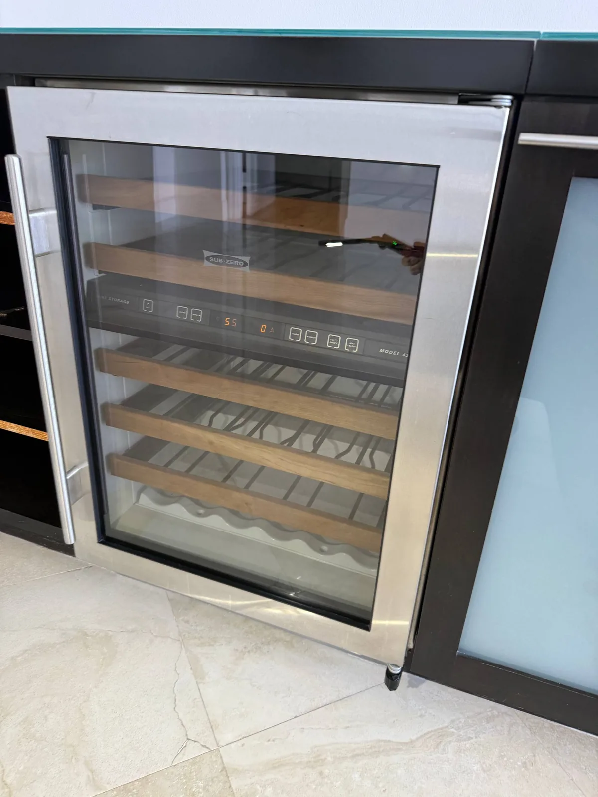A stainless steel Sub-Zero wine cooler with its glass door revealing wooden shelves inside