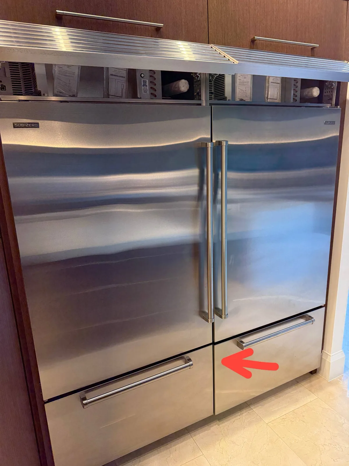 A stainless steel Sub-Zero refrigerator with its top ventilation grill pulled out, revealing components and some packaging