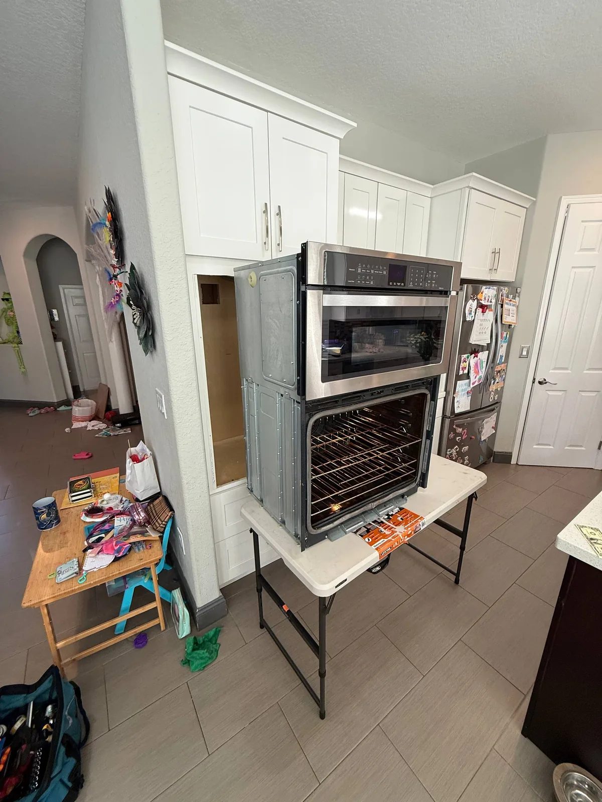 An oven and microwave combination unit is pulled out for repair, sitting on a table in a kitchen