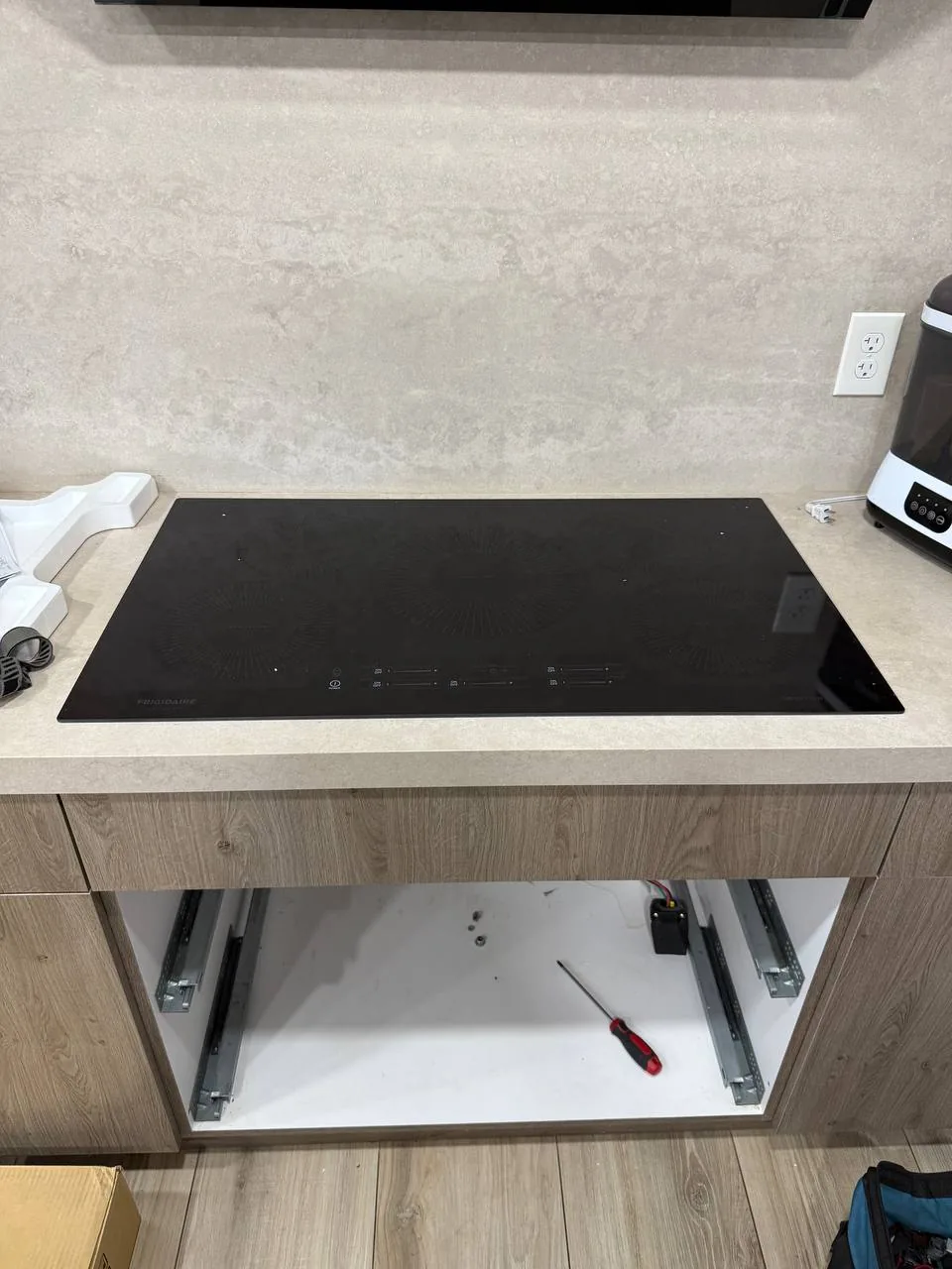 A cooktop is installed on a countertop with the drawer below removed, exposing a screwdriver and wires