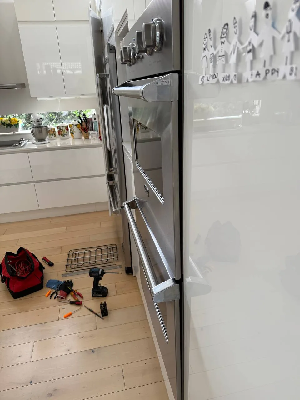 A stainless steel double oven with various tools laid out on the light wooden floor in front of it