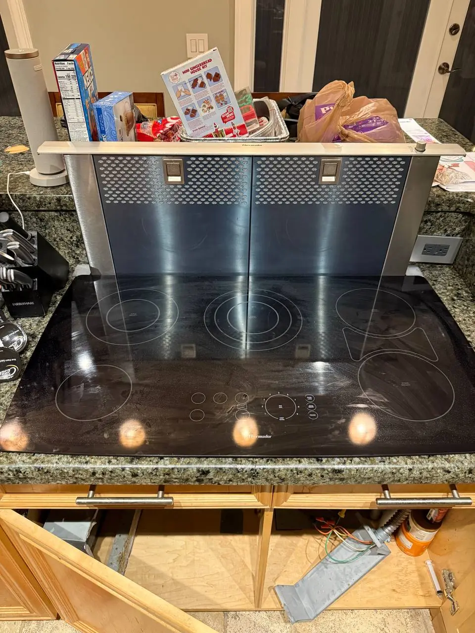 A Thermador cooktop and downdraft range hood, with open cabinetry below exposing wiring