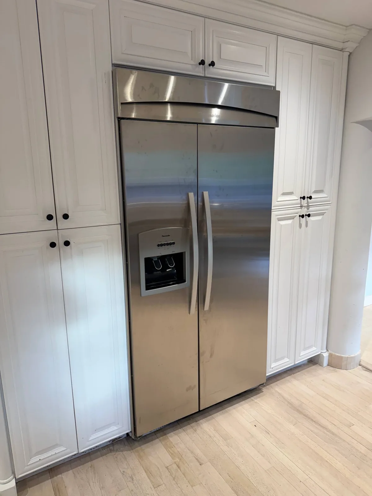 A stainless steel Thermador refrigerator built into white kitchen cabinets