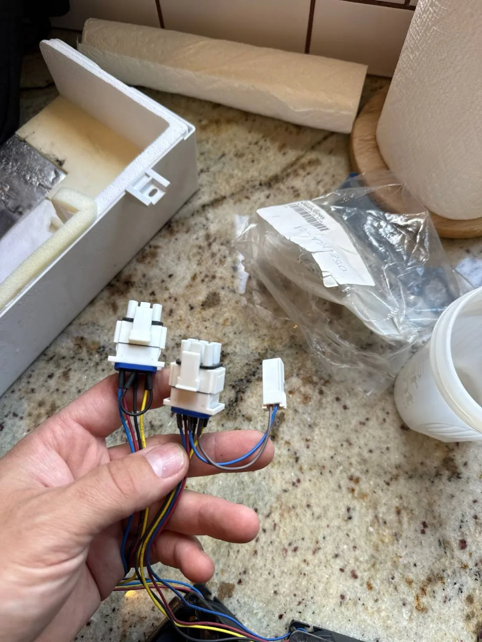 A technician's hand is holding electrical connectors for an ice maker on a granite countertop
