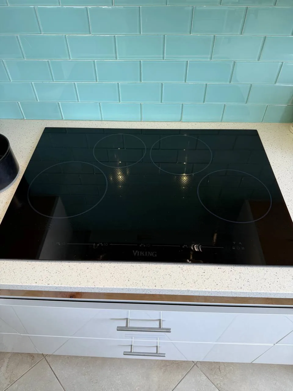 A black Viking induction cooktop is installed on a white countertop with a blue tile backsplash
