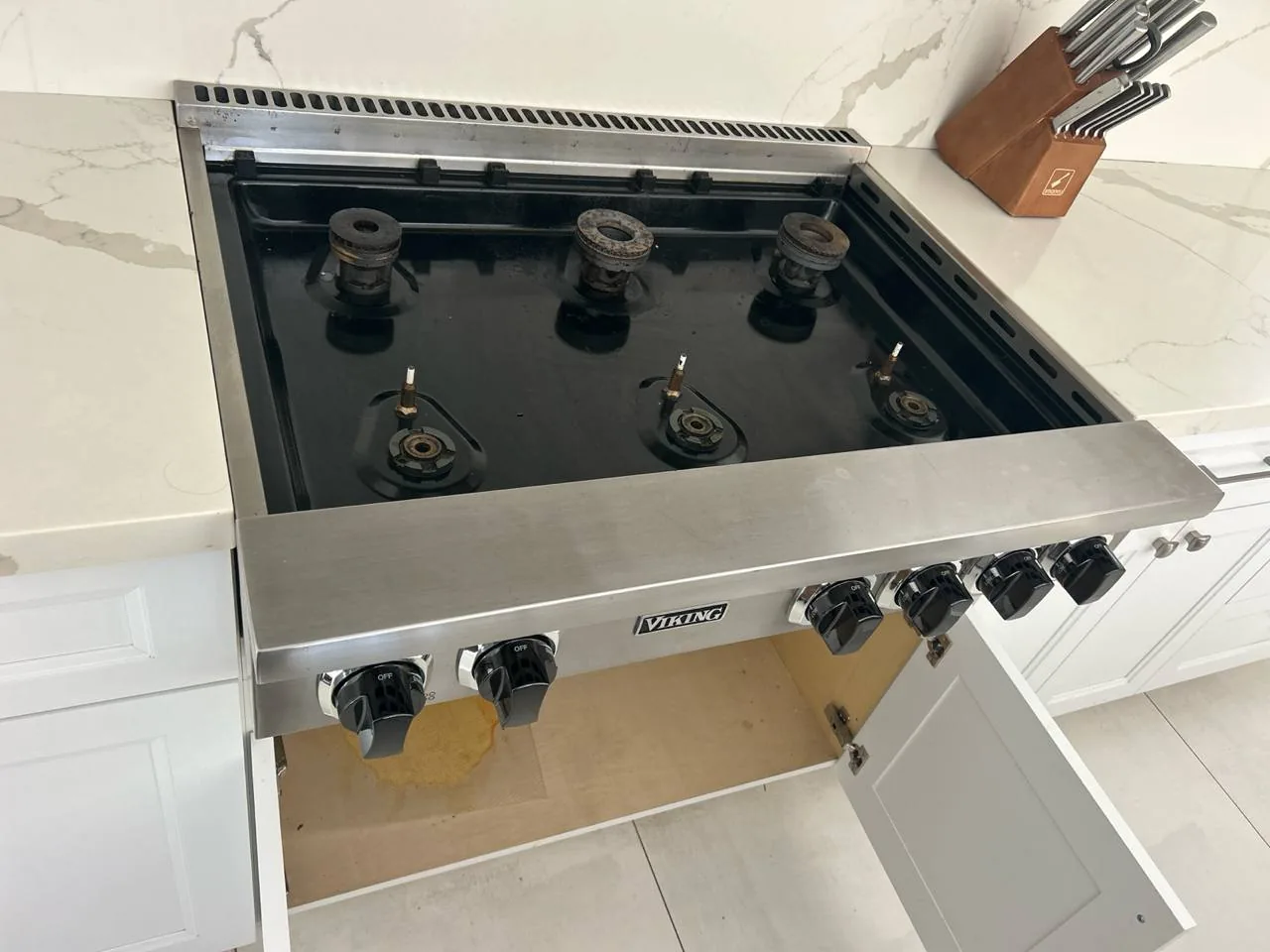 A Viking cooktop with all burners removed, showing the internal igniters and the brand logo on the front control panel, with