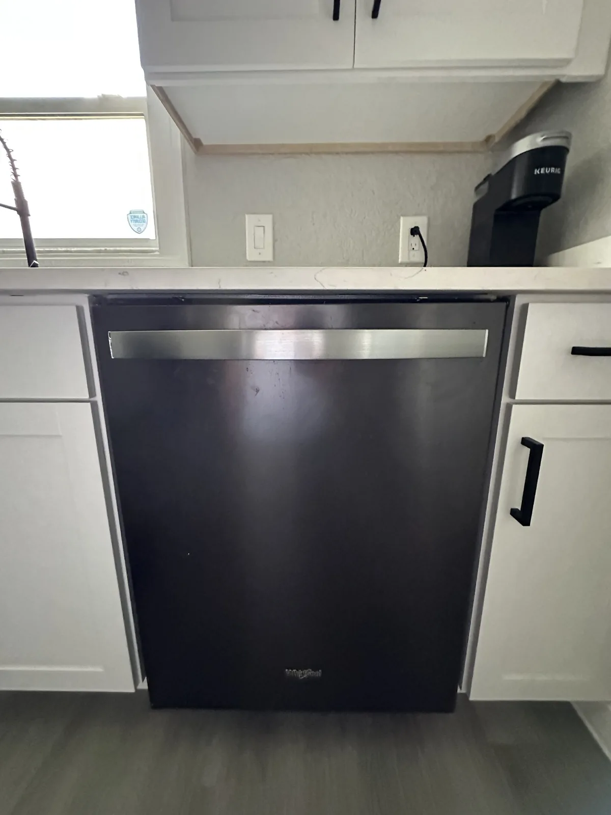 A dark Whirlpool dishwasher installed in a kitchen with white cabinets