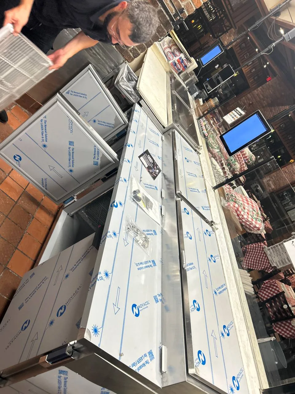 A technician is working on installing new stainless steel refrigeration units in a commercial kitchen