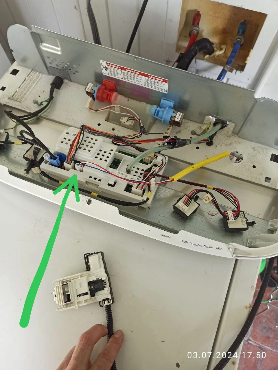 A washer with its top panel open, exposing wires and components, with a technician's hand holding a part