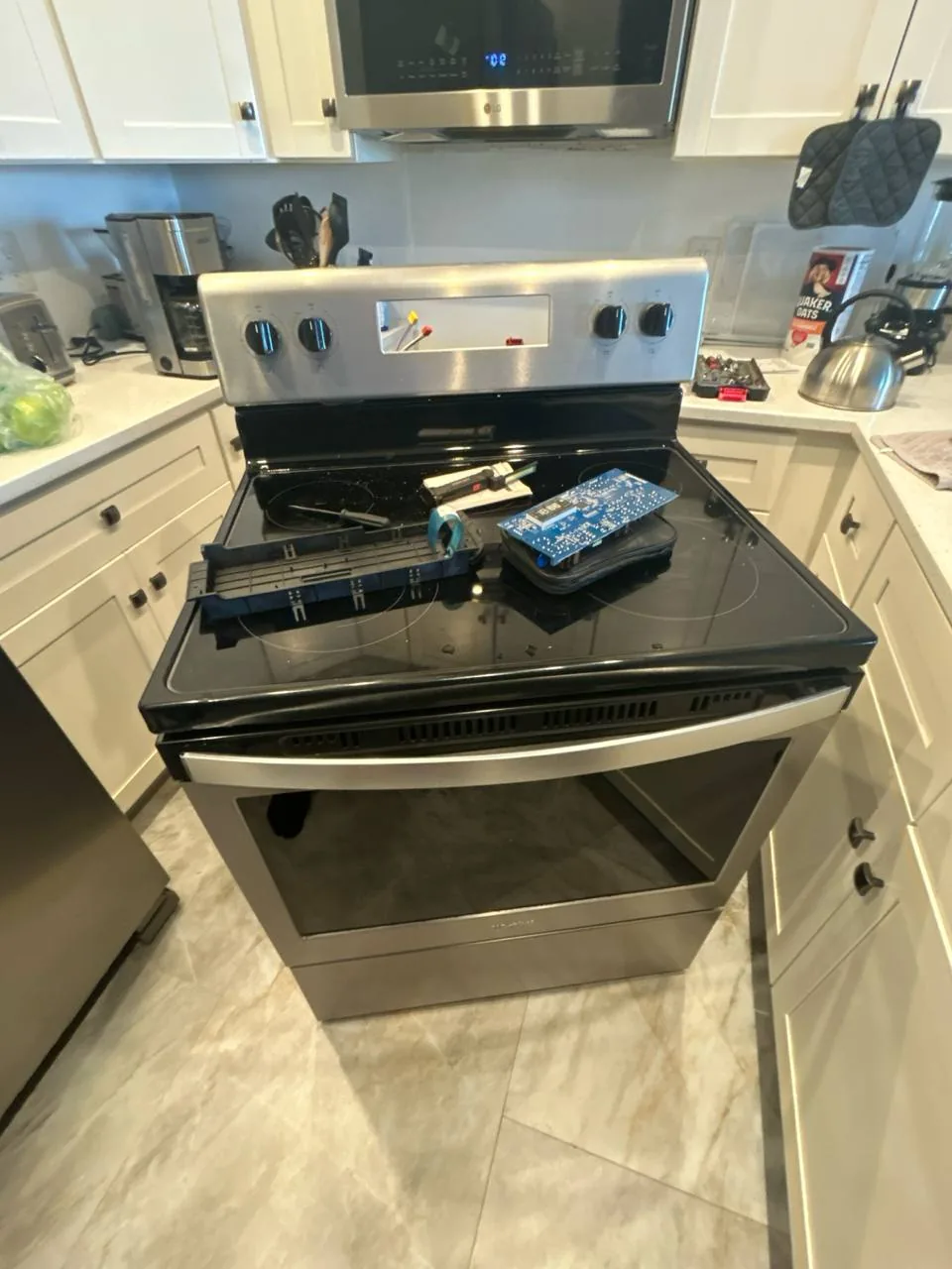 A stainless steel oven with its control panel disassembled and a circuit board resting on the cooktop