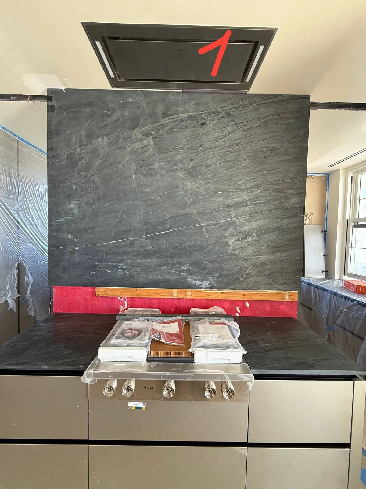 A new Wolf cooktop is installed on a dark stone countertop with a range hood above, in a room under construction