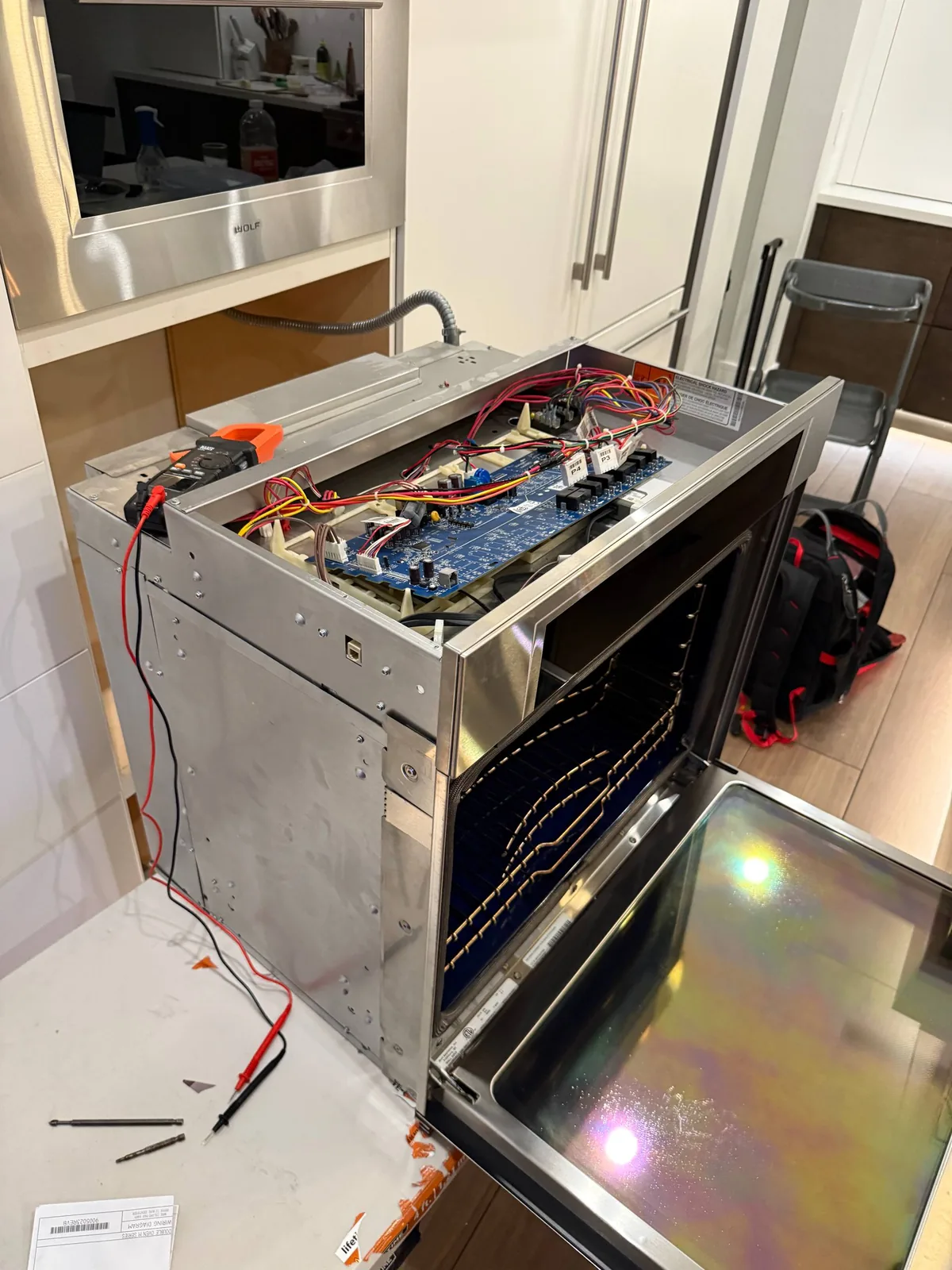 A Wolf oven with its top panel removed, revealing internal wiring and circuit boards during repair, with tools laid out on
