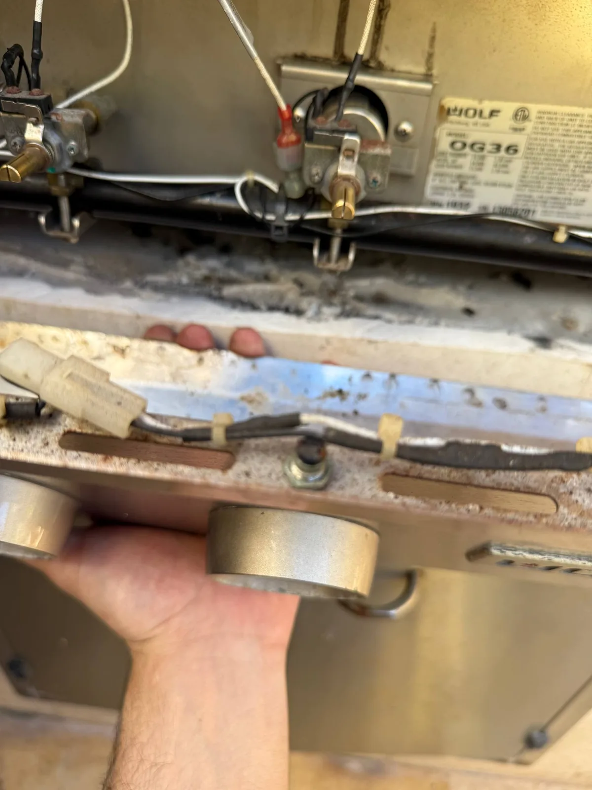 A technician's hand next to a Wolf cooktop with internal wiring and components exposed