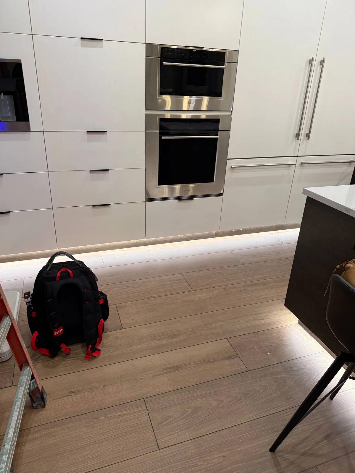 A kitchen scene featuring built-in Wolf ovens and a Milwaukee backpack on the floor