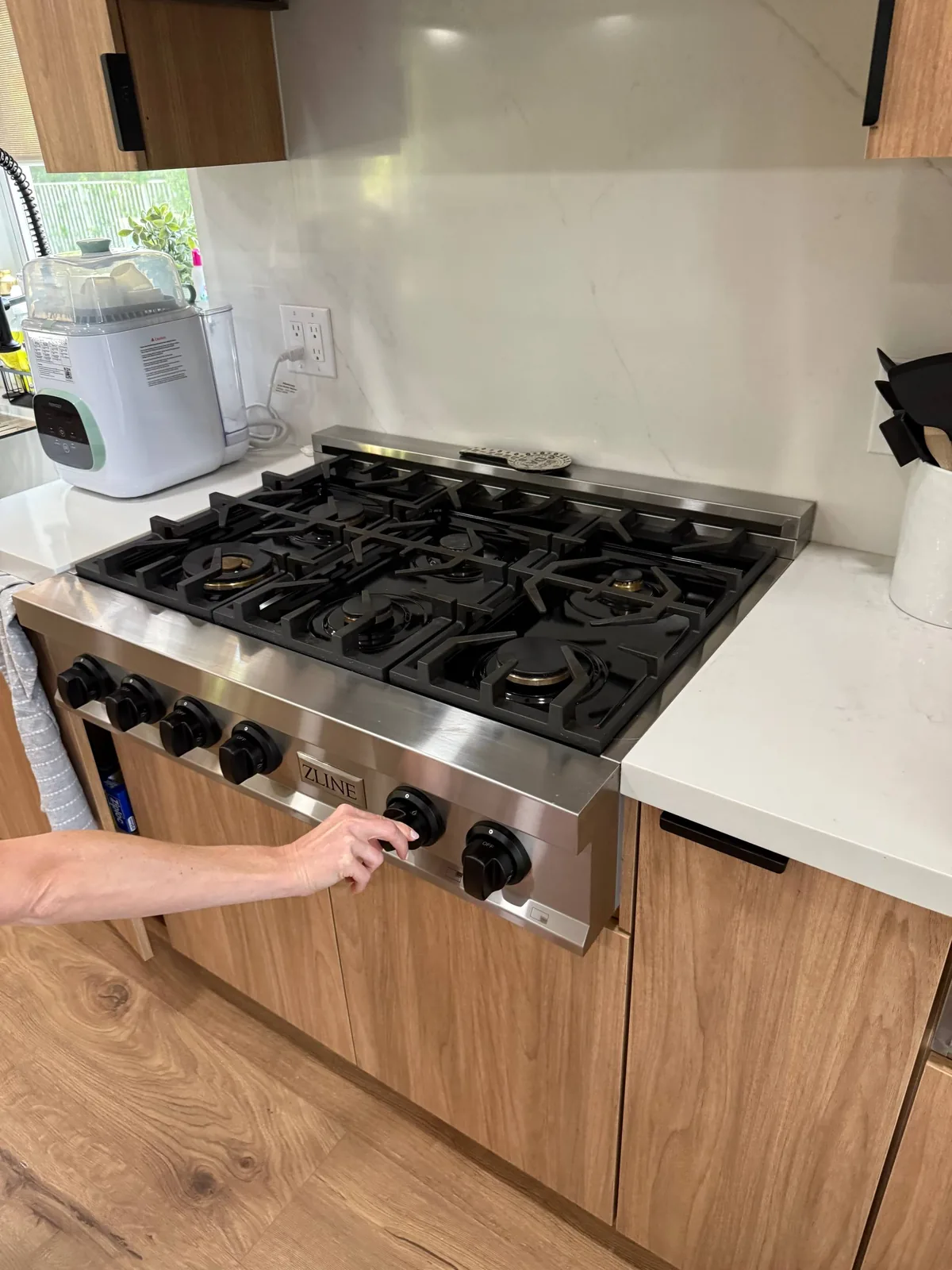 A hand adjusts the knob on a ZLINE cooktop in a modern kitchen